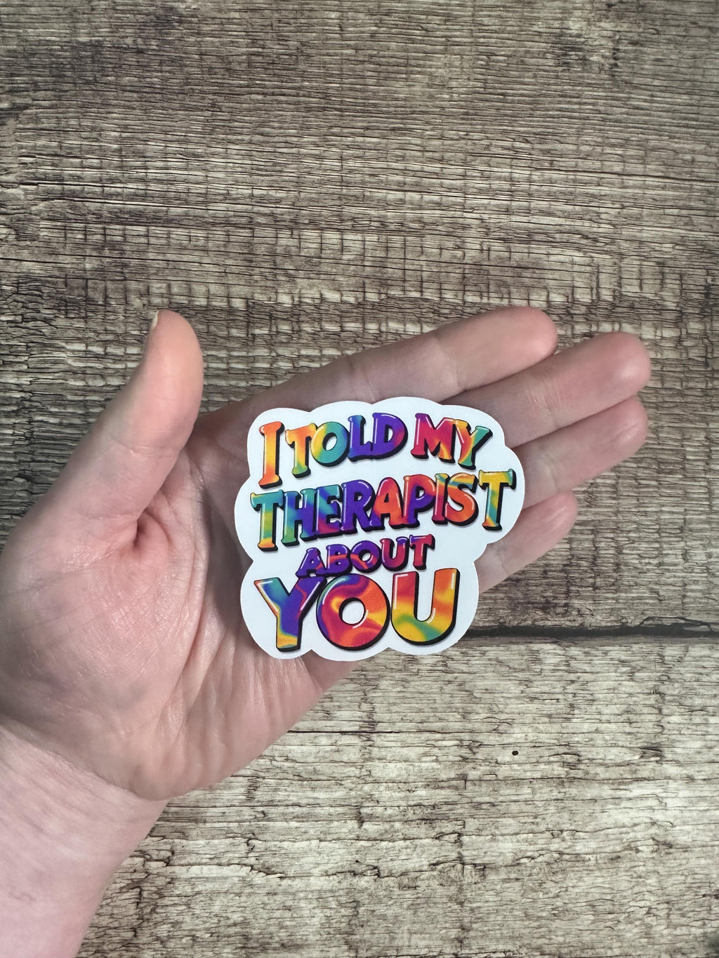 Hand holding a colorful sticker with text against a wooden background